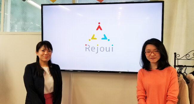 「理・情・意」の3つの意味を込めたRejouiのロゴの前での写真